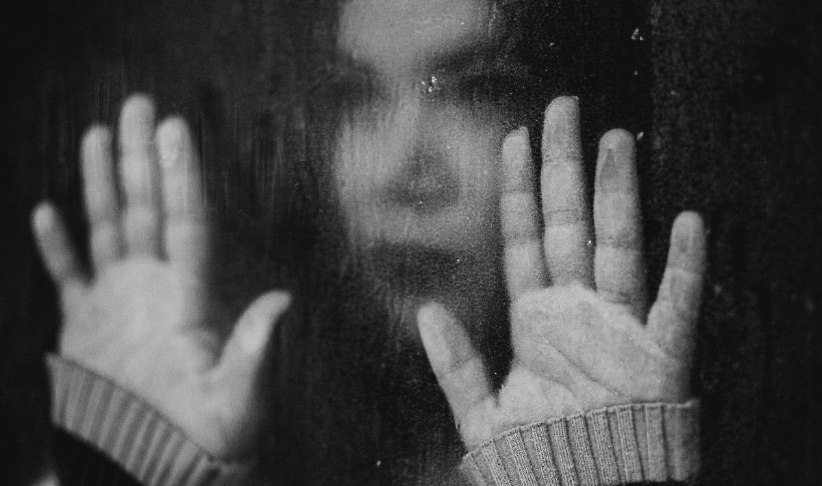 girl looking sad with hands against window